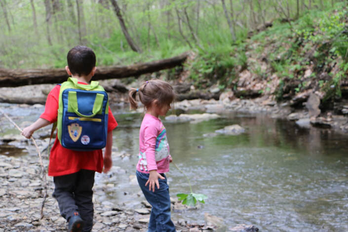 Boy and girl hiking by a creek in the woods.